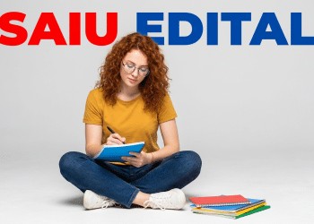 Jovem de cabelos cacheados escreve em caderno azul sentada no chão com cadernos ao lado e texto "SAIU EDITAL" acima