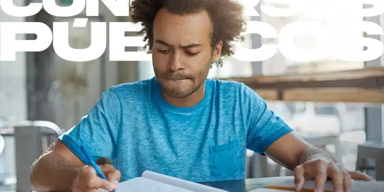 Homem jovem com cabelo afro, vestindo camiseta azul, concentrado escrevendo em um caderno com um livro aberto. Ao fundo, o texto sobreposto diz "Concursos Públicos".