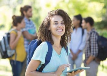 Estudante universitária sorridente segurando um tablet no campus, em alusão aos cursos universitários em alta no mercado de trabalho.