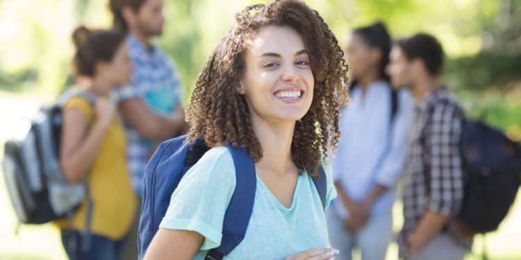 Estudante universitária sorridente segurando um tablet no campus, em alusão aos cursos universitários em alta no mercado de trabalho.