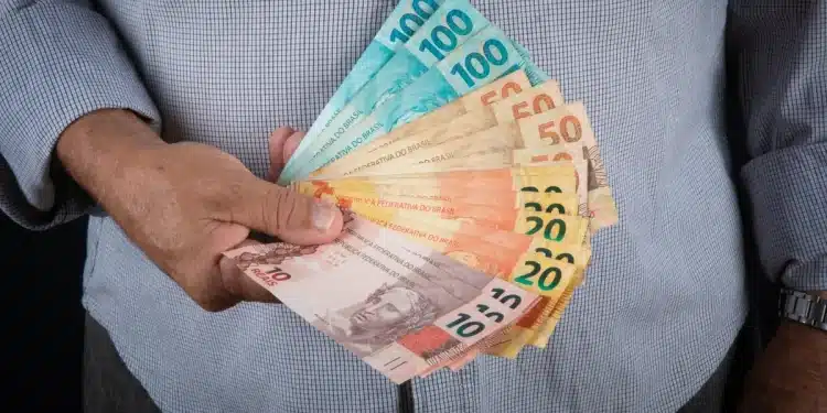 Notas de dinheiro com valores de R$ 10, R$20, R$50 e R$100, representando o 13º salário do INSS para aposentados e pensionistas que recebem acima de um salário mínimo.
