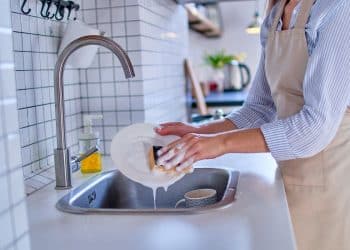 Pessoa lavando prato com esponja e detergente na pia da cozinha.