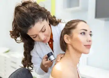 Dermatologista examinando a pele de uma paciente com dermatoscópio durante avaliação clínica.