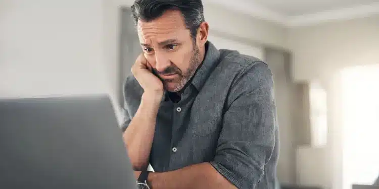 Homem preocupado olhando para o laptop em casa, lidando com o estresse, representando os desafios de carreira após os 40 anos.
