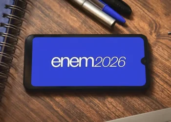 Tela de smartphone com o logo do Enem 2026 em fundo azul, com canetas e cadernos ao redor.