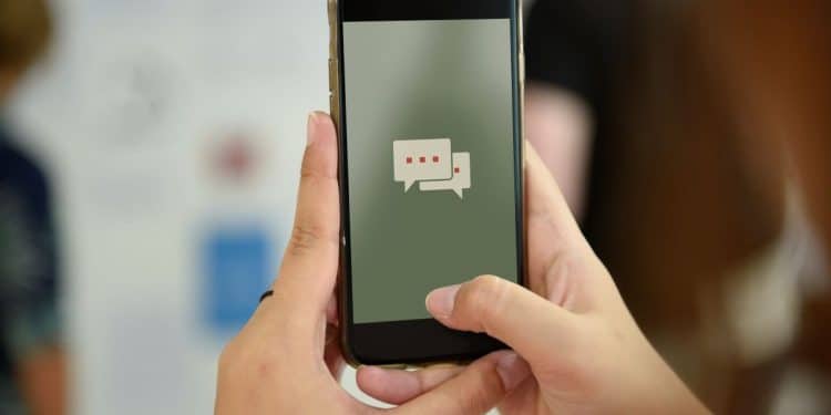 Pessoa segurando um smartphone com tela mostrando ícones de mensagens, simbolizando a comunicação digital.