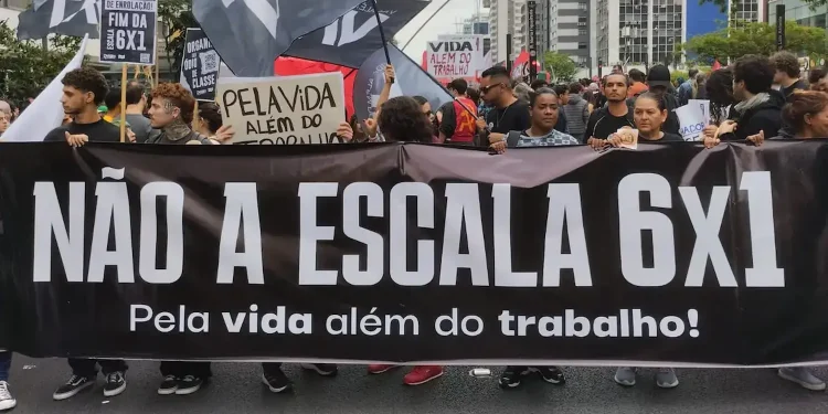 Manifestantes segurando faixa em protesto contra a escala 6x1, com bandeiras e cartazes sobre a vida além do trabalho.