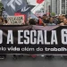 Manifestantes segurando faixa em protesto contra a escala 6x1, com bandeiras e cartazes sobre a vida além do trabalho.