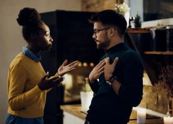 Casal em casa discutindo com gestos intensos, ilustrando conflito causado por opiniões e reações emocionais.