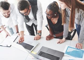 Equipe profissional reunida analisando dados em laptops durante reunião de trabalho colaborativa.