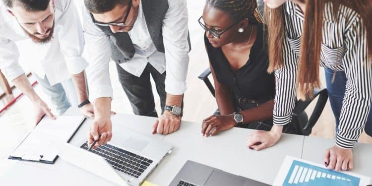 Equipe profissional reunida analisando dados em laptops durante reunião de trabalho colaborativa.