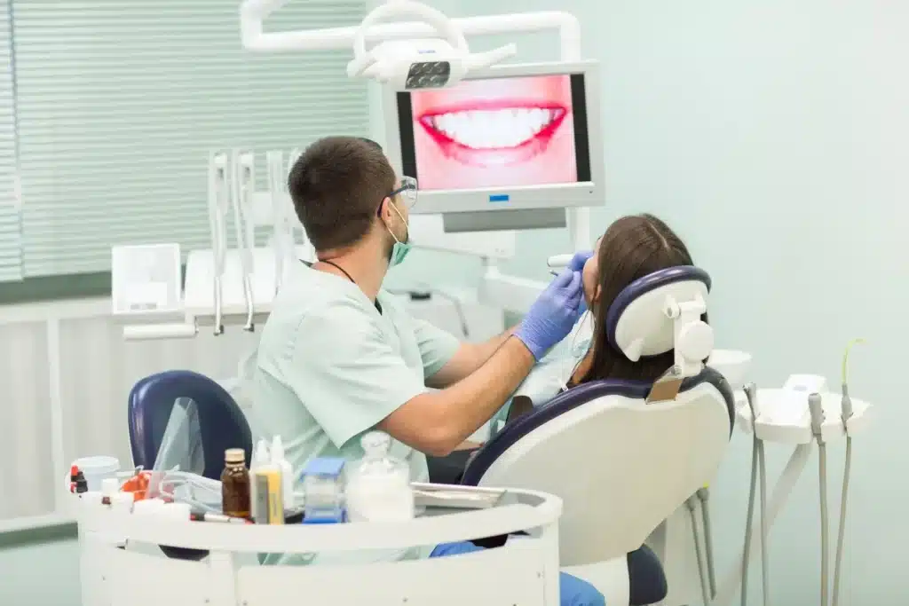 Dentista realizando exame em paciente no consultório odontológico enquanto exibe uma imagem de sorriso saudável na tela.