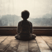 Silhueta de menino de costas, sentado no piso de madeira, observando janela grande com vidro embaçado pela chuva