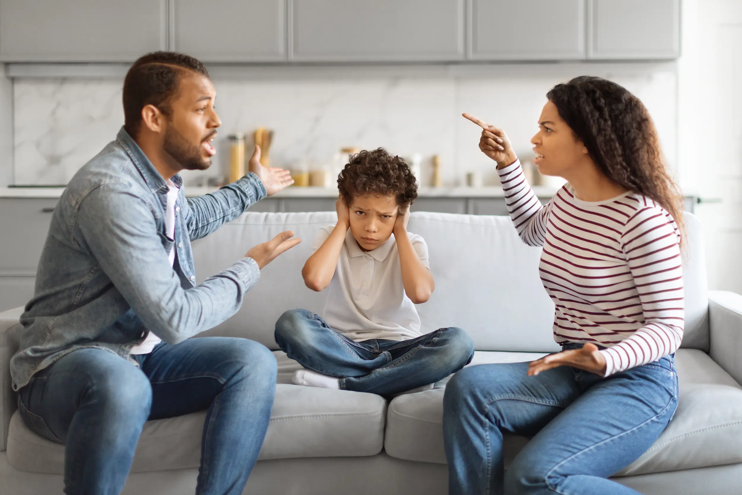 Criança com as mãos nos ouvidos, visivelmente angustiada, enquanto os pais discutem agressivamente ao fundo.