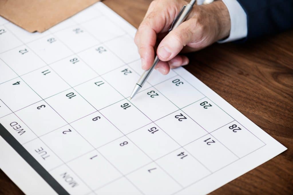 Feriados abril 2026 – pessoa apontando caneta em calendário sobre mesa de madeira