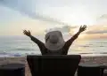 Mulher de costas desfrutando da vista do mar ao pôr do sol, representando momentos de descanso e relaxamento em viagens durante o mês de maio de 2026.