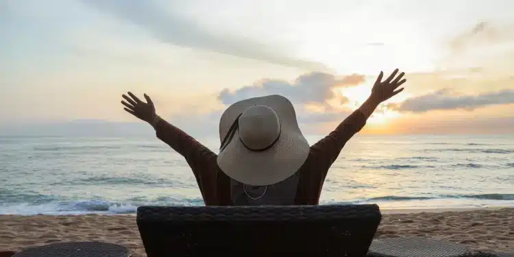 Mulher de costas desfrutando da vista do mar ao pôr do sol, representando momentos de descanso e relaxamento em viagens durante o mês de maio de 2026.