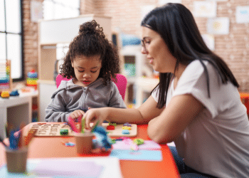 Professora auxiliando criança pequena em atividade pedagógica com peças coloridas em sala de aula