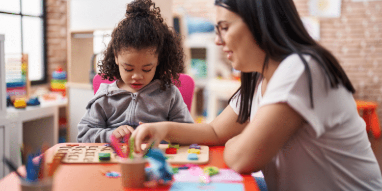 Professora auxiliando criança pequena em atividade pedagógica com peças coloridas em sala de aula