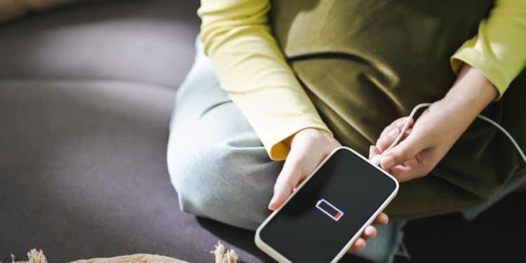 Celular com bateria baixa sendo conectado ao carregador por uma pessoa sentada no sofá.