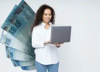 Mulher sorrindo enquanto trabalha no computador com notas de 100 reais ao fundo, ilustrando a possibilidade de ganhar mais de R$ 6 mil em profissões home office sem diploma.