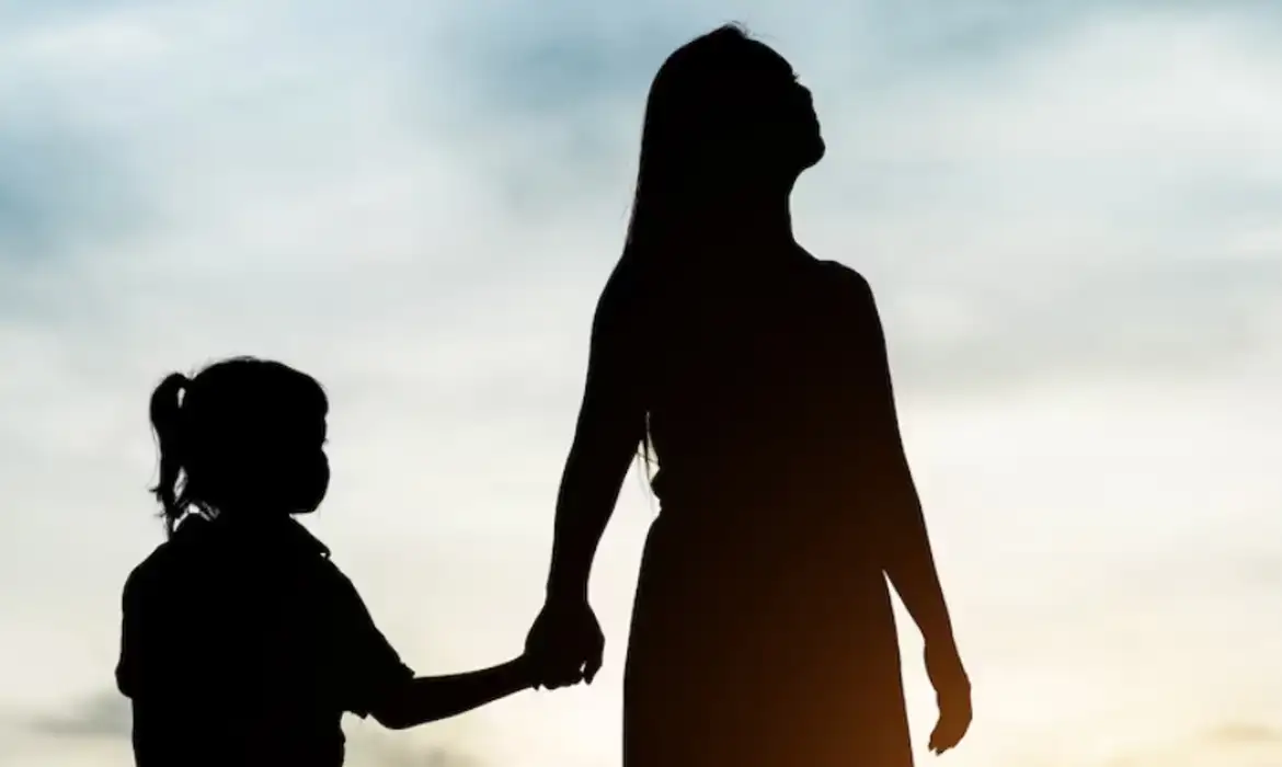 Silhueta de mãe e filha de mãos dadas ao pôr do sol, em alusão às características genéticas herdadas pela linhagem materna.