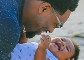 Pai segurando bebê sorridente no colo, em alusão às características genéticas herdadas pela linhagem paterna.