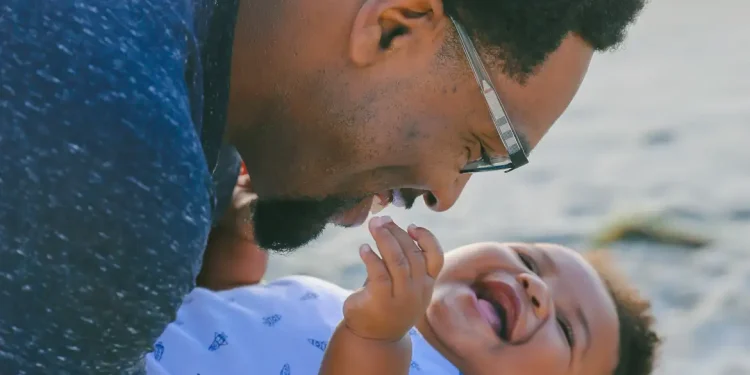 Pai segurando bebê sorridente no colo, em alusão às características genéticas herdadas pela linhagem paterna.