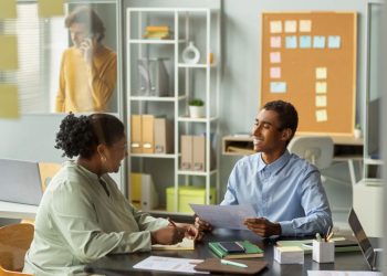 Dois profissionais conversando em um ambiente de escritório, representando habilidades comportamentais como comunicação, relacionamento interpessoal e trabalho em equipe