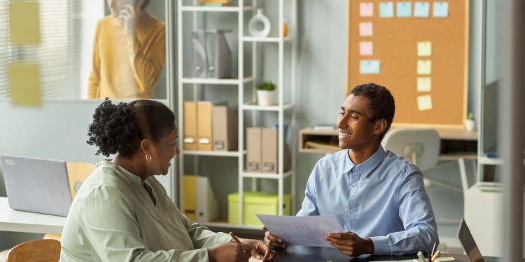 Dois profissionais conversando em um ambiente de escritório, representando habilidades comportamentais como comunicação, relacionamento interpessoal e trabalho em equipe