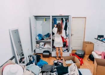 Acumulação de coisas psicologia - mulher de costas diante de guarda-roupa lotado com roupas e objetos espalhados pelo quarto