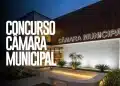 Fachada iluminada da Câmara Municipal em período noturno com jardim ornamental e bancos de concreto em primeiro plano