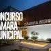 Fachada iluminada da Câmara Municipal em período noturno com jardim ornamental e bancos de concreto em primeiro plano