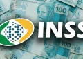 Logo do INSS sobre notas de 100 reais, relacionado ao pagamento do benefício de R$ 2.431,50 em 2026.