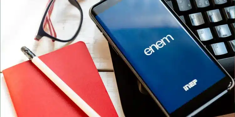 Celular com logo do Enem Inep ao lado de caderno vermelho e óculos, representando a isenção da taxa de inscrição do Enem 2026