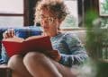 Mulher lendo livro em casa com expressão concentrada, representando leitura profunda e foco cognitivo.