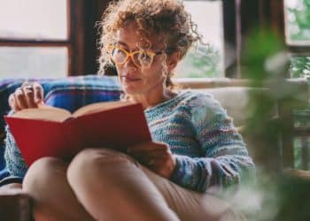 Mulher lendo livro em casa com expressão concentrada, representando leitura profunda e foco cognitivo.