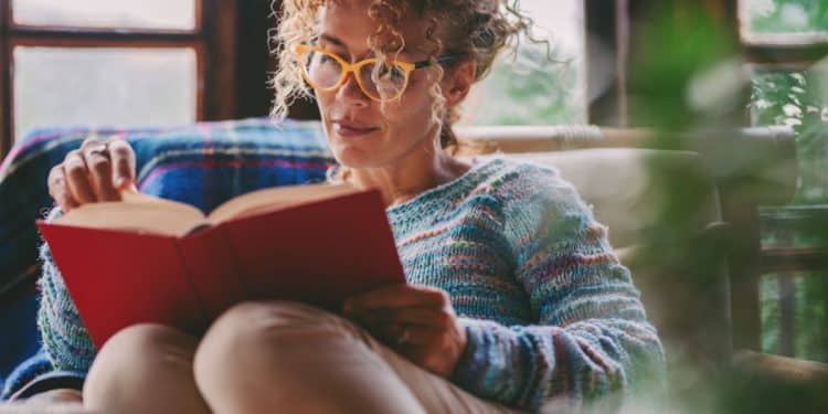 Mulher lendo livro em casa com expressão concentrada, representando leitura profunda e foco cognitivo.