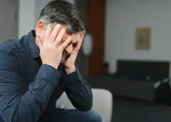 Homem com expressão de angústia segurando a cabeça, representando o medo de passar necessidade e ansiedade financeira