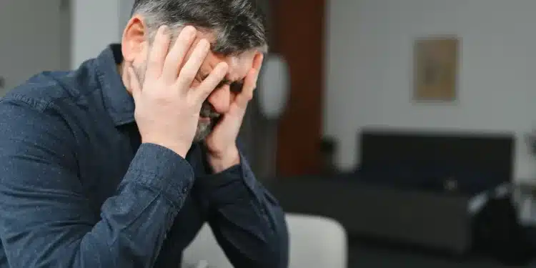 Homem com expressão de angústia segurando a cabeça, representando o medo de passar necessidade e ansiedade financeira