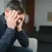 Homem com expressão de angústia segurando a cabeça, representando o medo de passar necessidade e ansiedade financeira