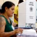 Mesária e eleitores em cabine de votação durante as eleições, destacando os mesários no processo eleitoral.