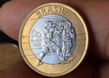 Close-up detalhado da moeda bimetálica de 1 real das Olimpíadas do Rio 2016 com o tema do Boxe, mostrando dois atletas em combate no ringue e a marca dos anéis olímpicos.