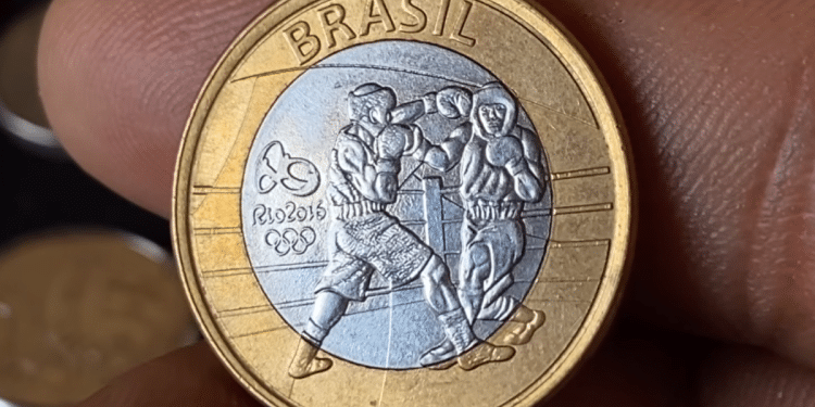 Close-up detalhado da moeda bimetálica de 1 real das Olimpíadas do Rio 2016 com o tema do Boxe, mostrando dois atletas em combate no ringue e a marca dos anéis olímpicos.