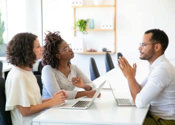 Três pessoas discutindo em uma reunião de trabalho, representando a comunicação no ambiente corporativo.