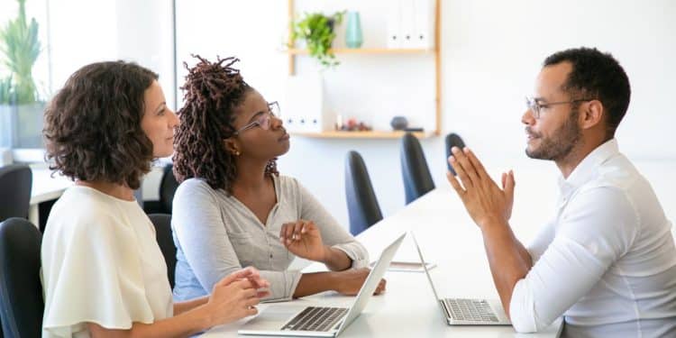 Três pessoas discutindo em uma reunião de trabalho, representando a comunicação no ambiente corporativo.