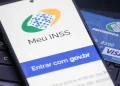 Celular exibindo a tela de login do aplicativo Meu INSS ao lado de cartão da Previdência Social, representando a consulta ao 13º salário com as mudanças de valores e isenção de IR em 2026