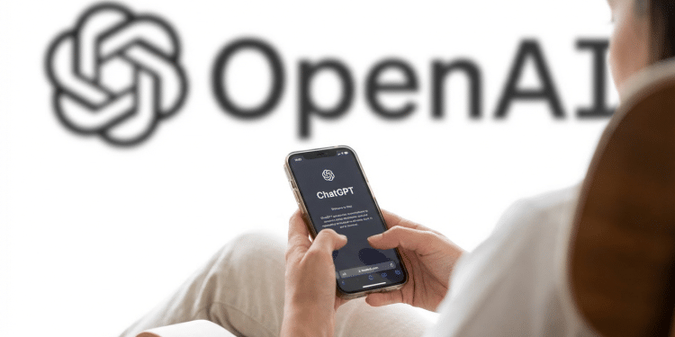 Pessoa segurando iPhone com tela de boas-vindas do ChatGPT, logo da OpenAI ao fundo em parede branca