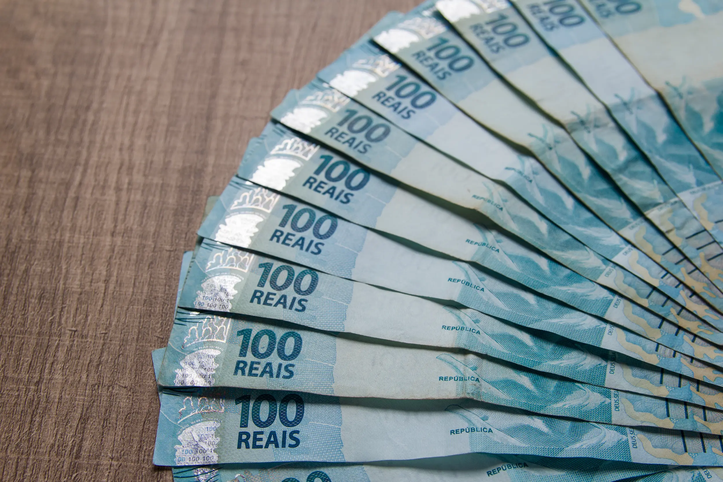 Notas de R$ 100 em fileira, representando o pagamento de benefícios.