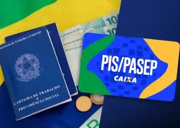 Carteira de Trabalho azul, notas de R$100 e cartão PIS/PASEP Caixa com bandeira do Brasil ao fundo